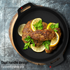 Black cast iron skillet with meat patties and lemon slices on a gray surface