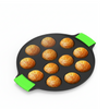 Black takoyaki pan with green handles containing golden-brown takoyaki on a white background