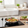 Stainless steel frying pan with vegetables on a stove in a kitchen setting