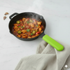 Black frying pan with green handle containing a colorful stir-fry on a light gray background