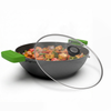 Black wok with green handles and a clear lid filled with food on a white background